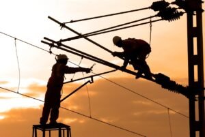 Electricians repairing power lines at sunset, showcasing teamwork and safety.