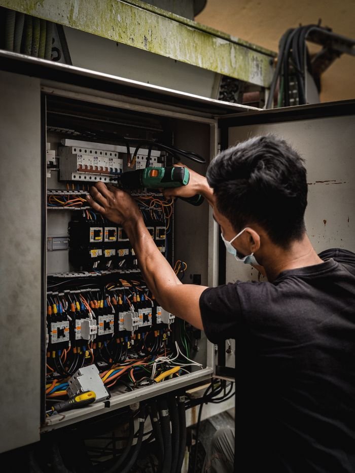 THERMAL SCANNING Technician working on circuit breaker panel, adjusting electrical wires indoors.